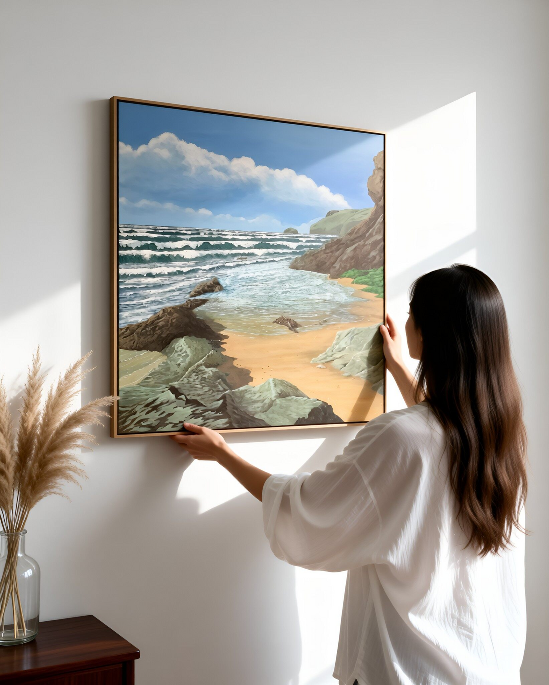 A woman positions a framed canvas print of a seascape